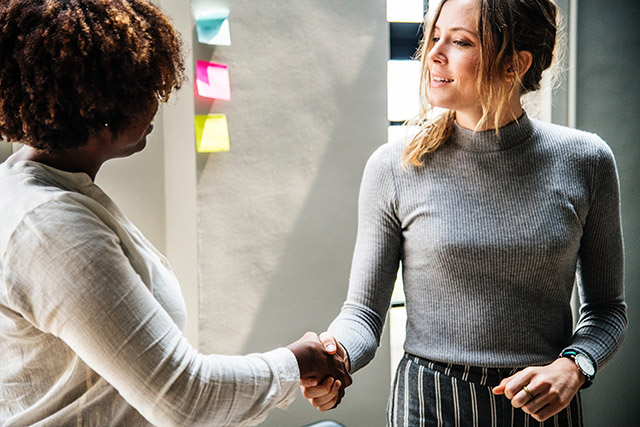 Two women shaking hands next to a wall with sticky notes